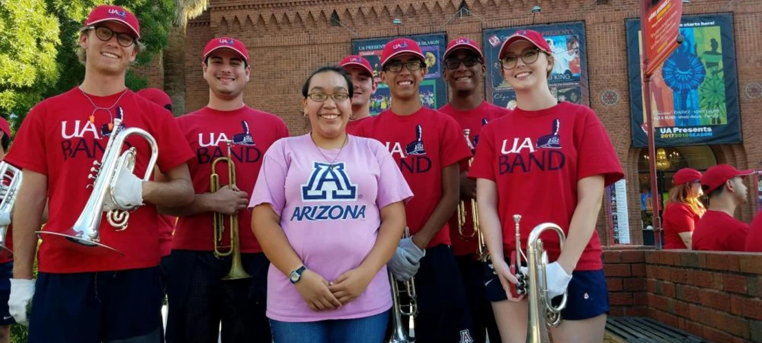 female student posing with UArizona marching band during pep rally